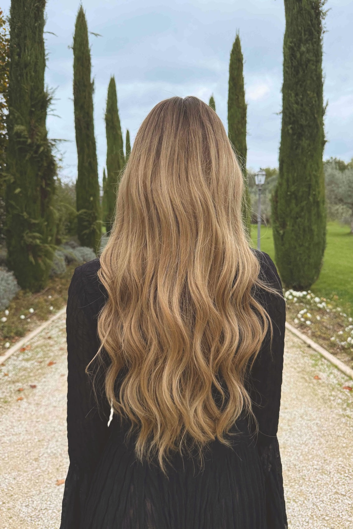 Woman wearing a BHBD Noble Nightshade wig. Long wig with dark blonde roots that transitions into slightly lighter lengths.